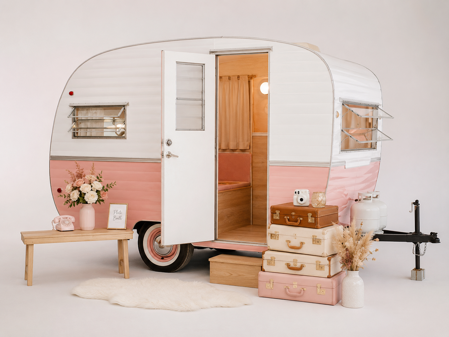 Vintage blush-and-white camper photo booth styled with flowers, suitcases, and elegant wedding décor.
